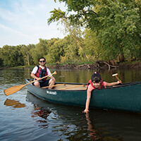 3M PFAS Settlement Two people in a canoe paddling on a river.